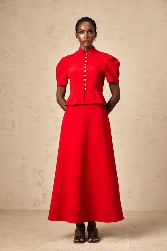 Woman wearing a red pleated blouse and matching skirt set standing against a plain background