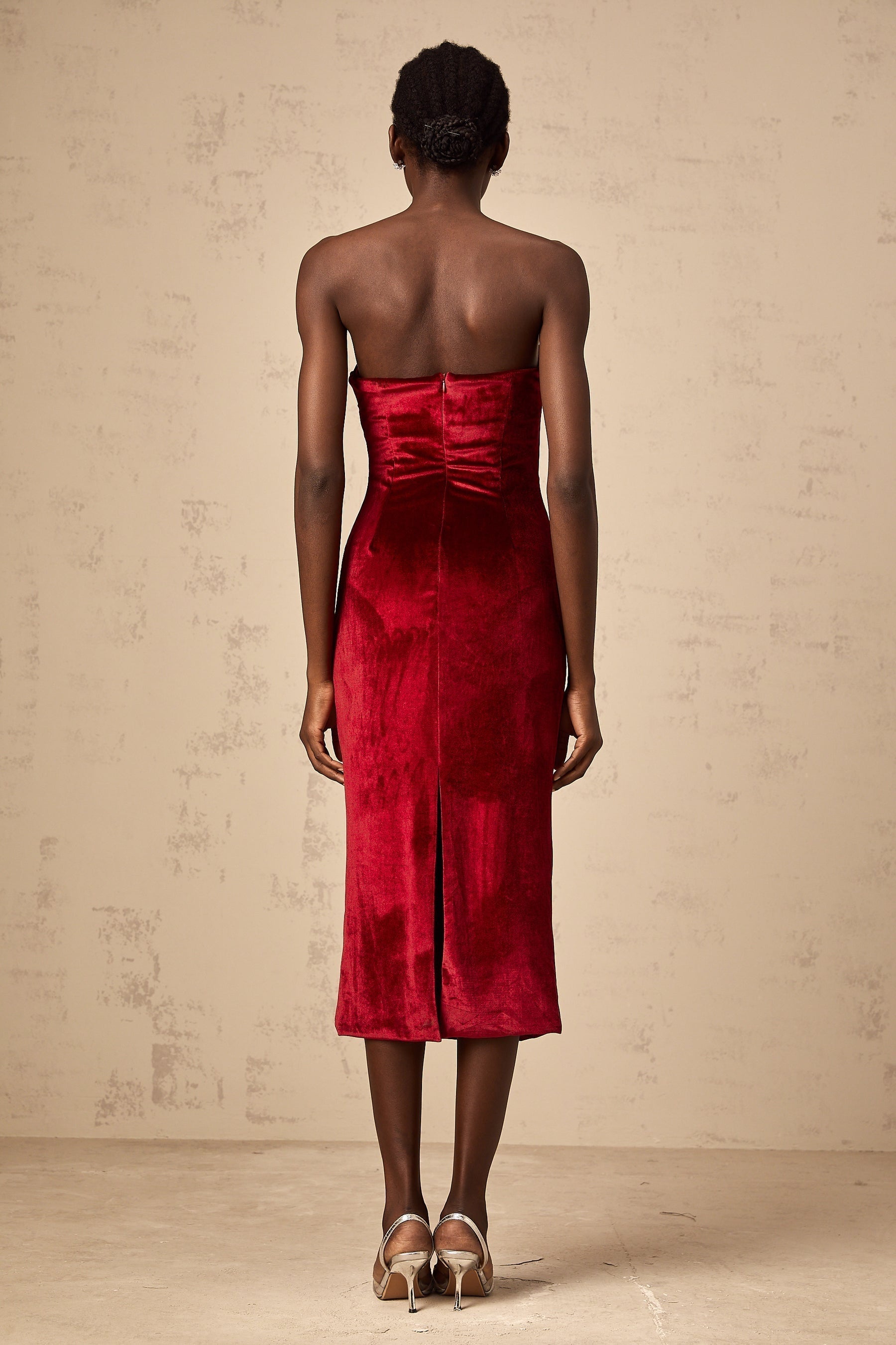 Woman wearing a red velvet midi dress with gathered details standing against a plain background