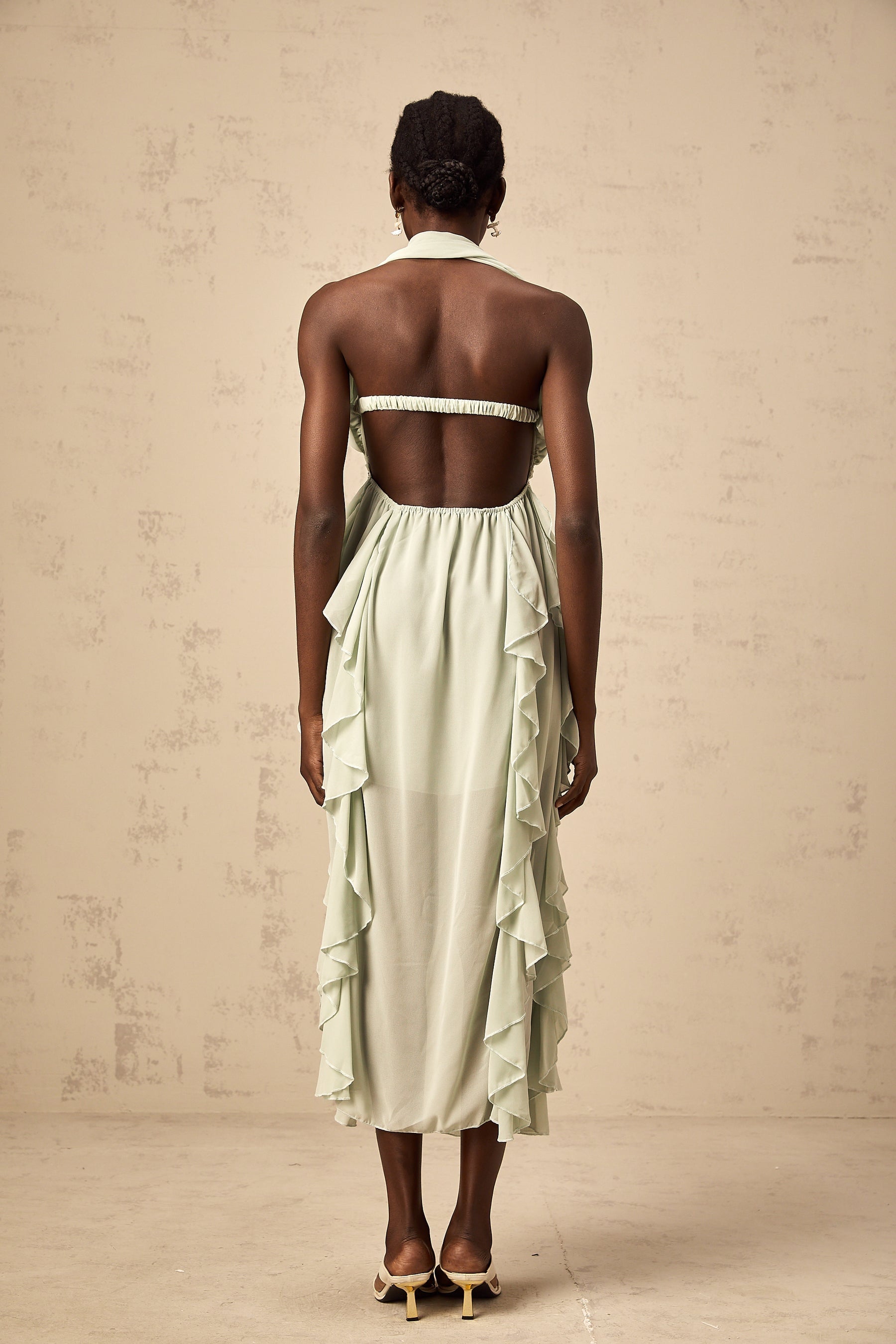 Woman wearing a ruffled midi dress with embellishments and a flowy silhouette in a soft color