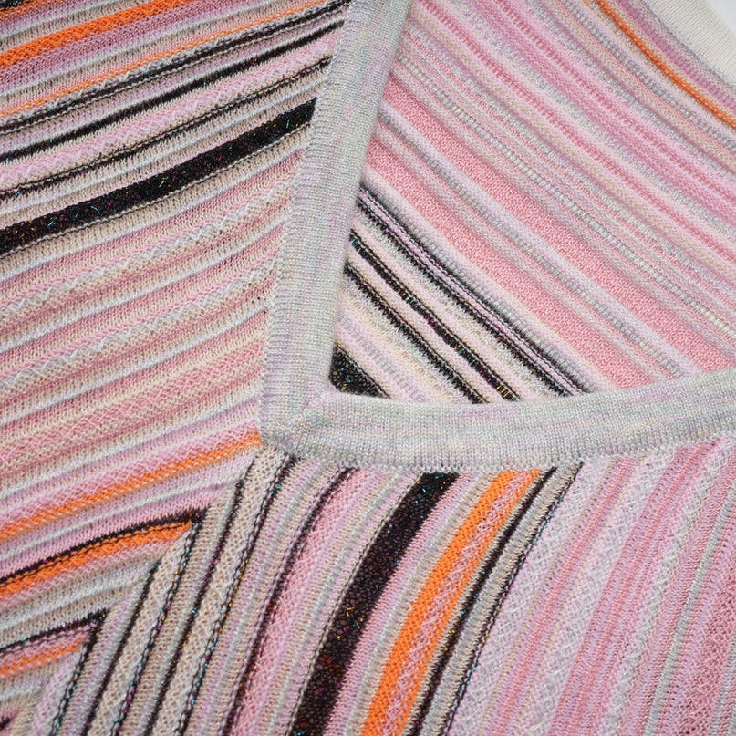 Woman wearing a shiny pink pleated midi dress with metallic sheen standing in a neutral background