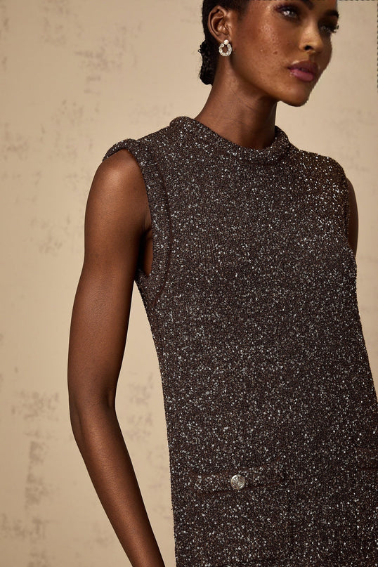 Woman wearing a short barley brown dress with sequin detailing and knit fabric standing against a plain background