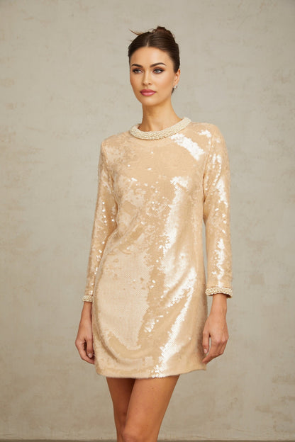 Woman wearing a short beige dress with faux pearl and sequin embellishments