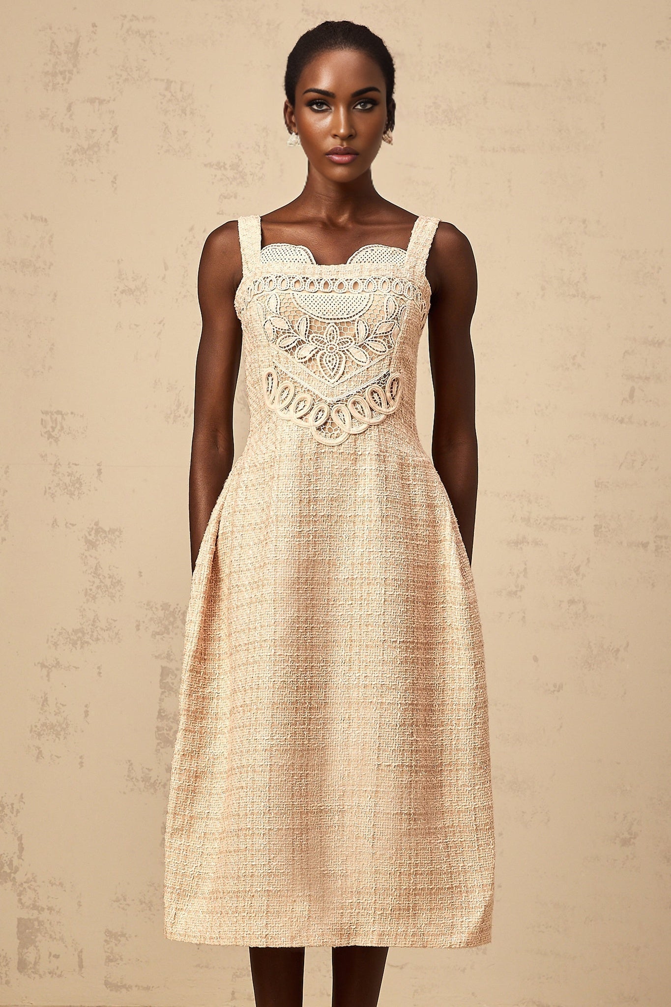 Woman wearing a short beige dress with intricate embroidery pattern standing against a neutral background
