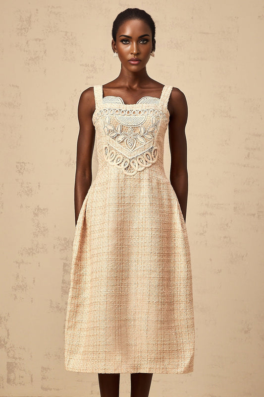 Woman wearing a short beige dress with intricate embroidery pattern standing against a neutral background