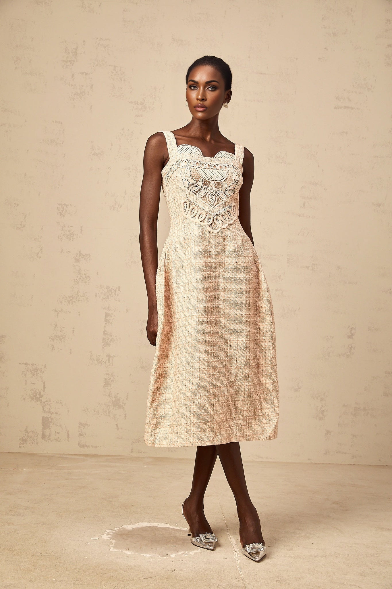 Woman wearing a short beige dress with intricate embroidery patterns standing against a plain background
