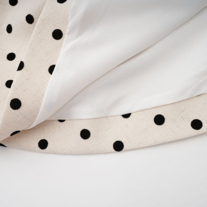 Woman wearing a short beige dress with white polka dots and puff sleeves standing against a plain background