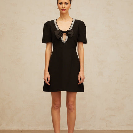 Woman wearing a short black dress with bow detail