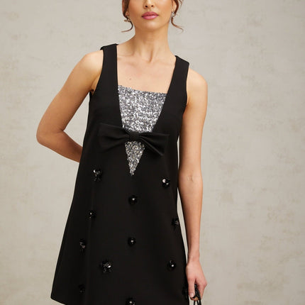 Woman wearing a short black dress with shimmering 3d floral sequin details on the fabric