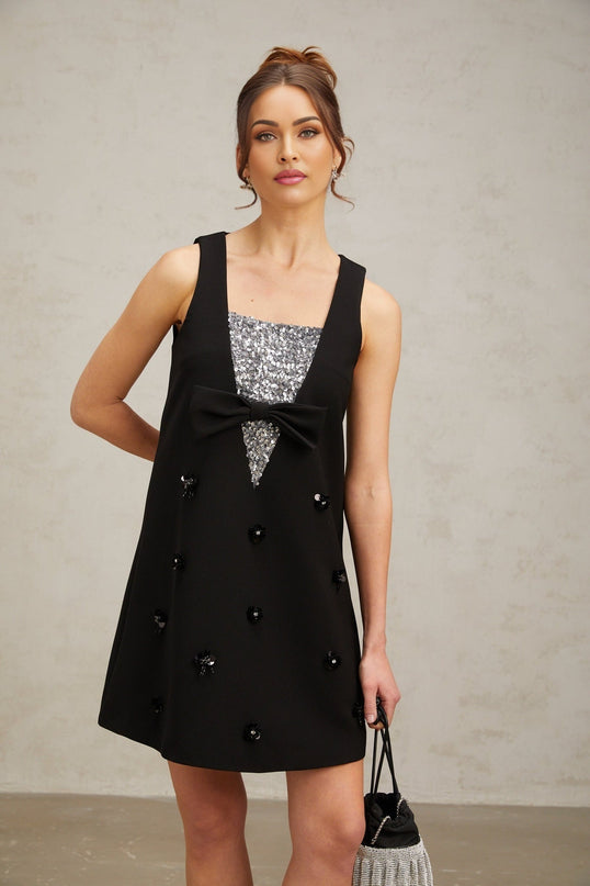 Woman wearing a short black dress with shimmering 3d floral sequin details on the fabric