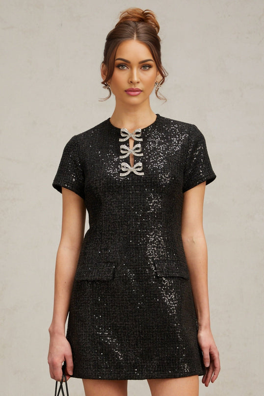 Woman wearing a short black mini dress with glitter detail and fitted silhouette