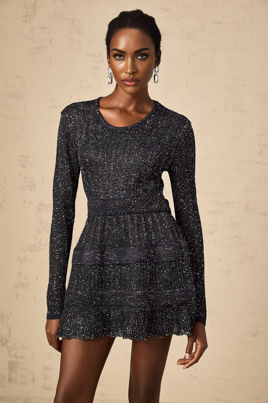 Woman wearing a short black mini dress with sequin embellishments and knit texture
