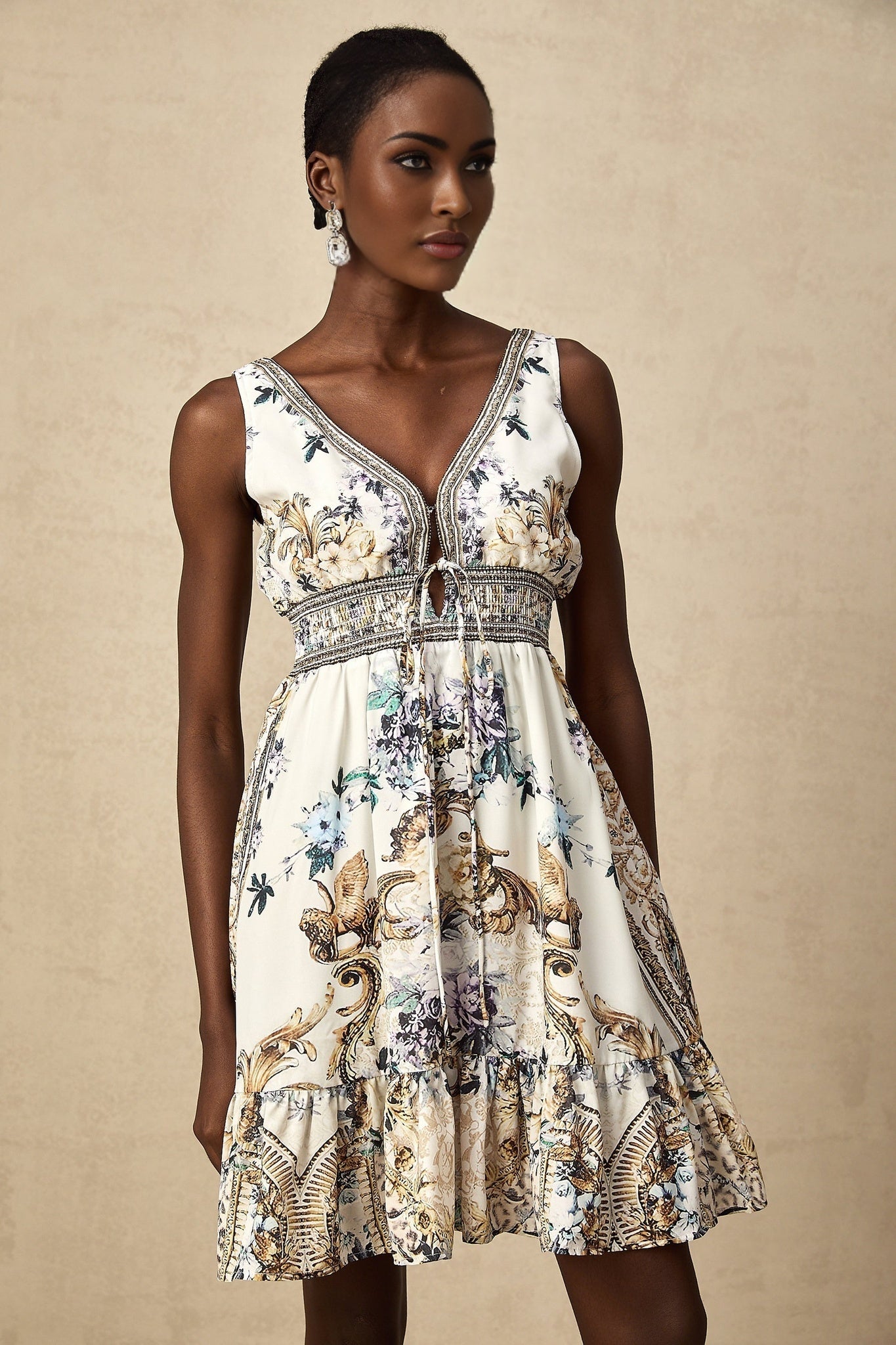 Woman wearing a short floral print dress with vneck in vibrant colors against a plain background
