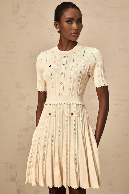 Woman wearing a short neutral colored knit dress with pleated skirt and delicate pointelle trim detail