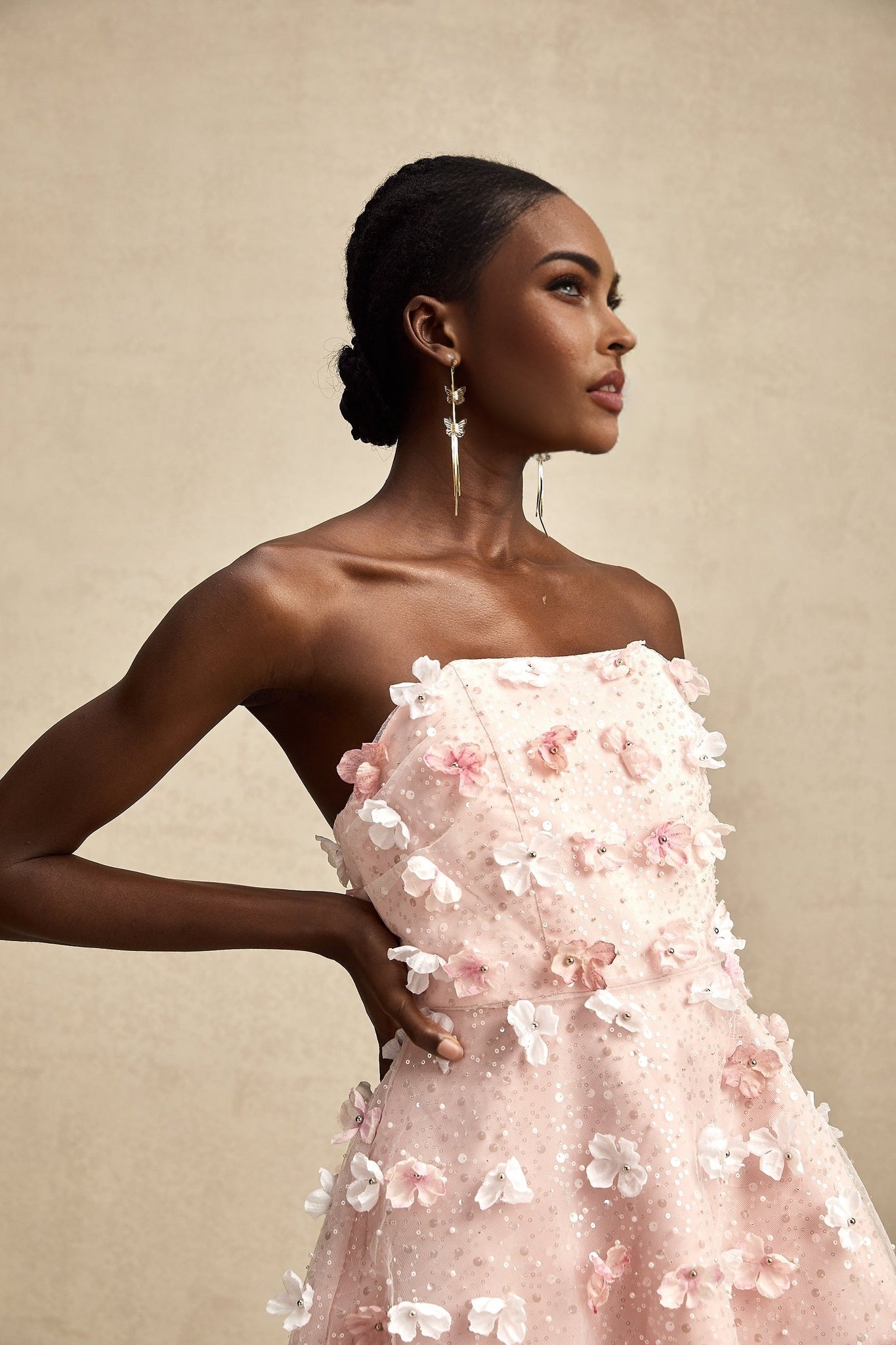 Woman wearing a short pink dress with three dimensional floral petal details and puffy sleeves standing against a plain background