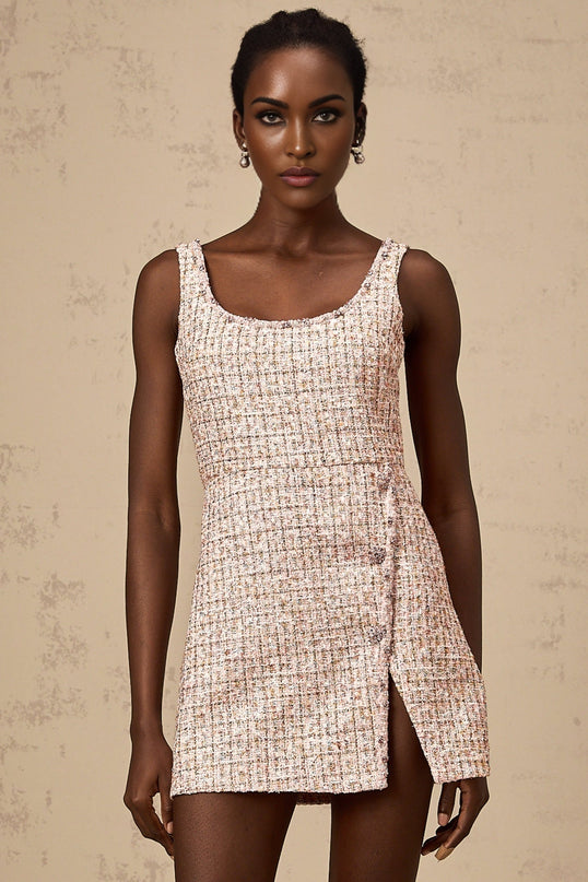 Woman wearing a short pink tweed dress with embellishments and decorative details standing in a neutral background