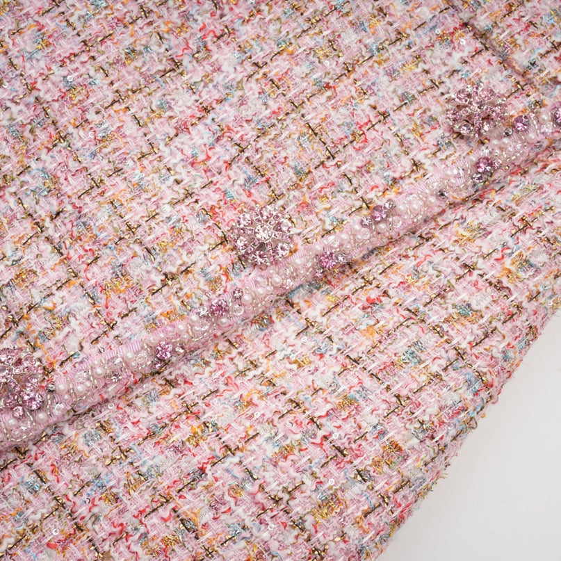 Woman wearing a short pink tweed dress with embellishments standing against a plain background