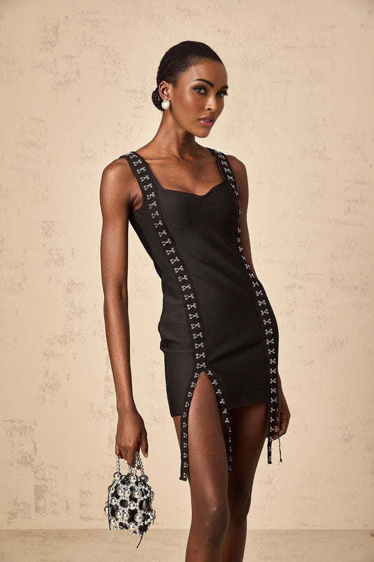 Woman wearing a short tight fitting black bandage dress with hook and eye closures