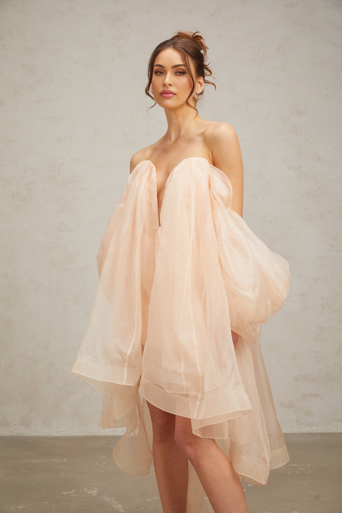 Woman wearing a short voluminous dress with bow details and puffed sleeves in a light color