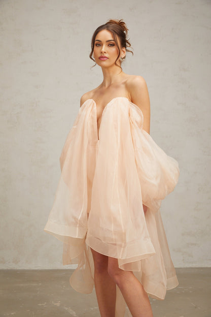 Woman wearing a short voluminous dress with bow details and puffed sleeves in a light color