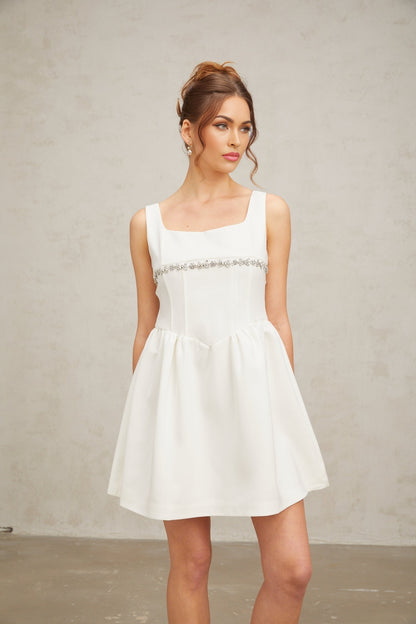 Woman wearing a short white dress with crystal embellishments and a fitted silhouette