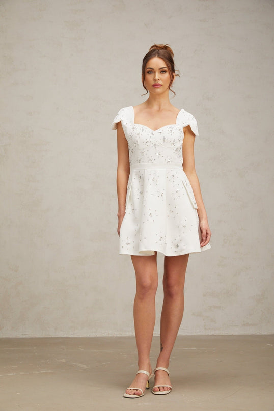 Woman wearing a short white dress with flared skirt and embellished details