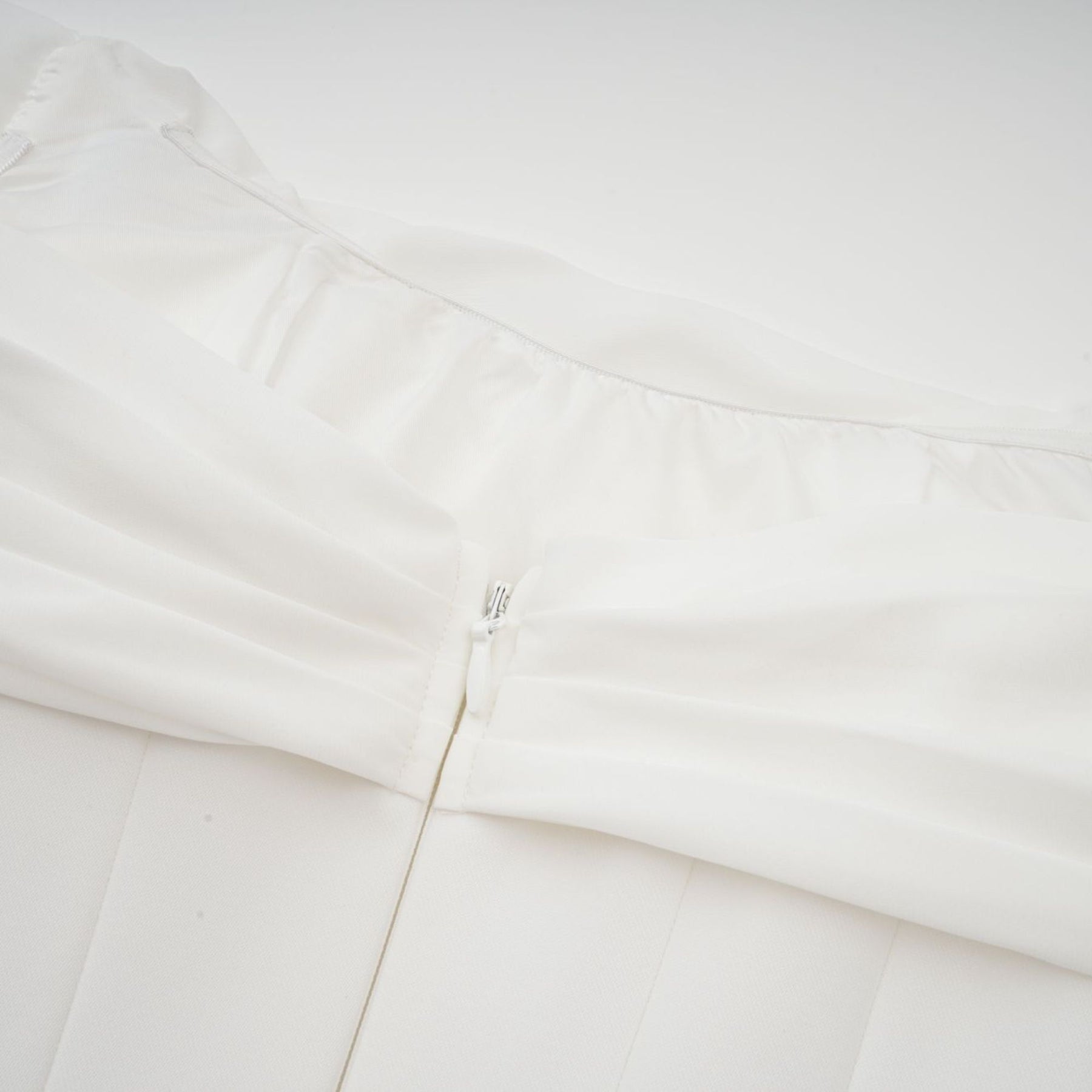 Woman wearing a short white dress with ruched fabric and ribbon design details