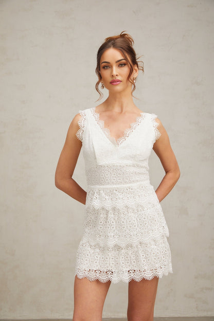 Woman wearing a short white lace dress with tiered skirt and delicate floral pattern