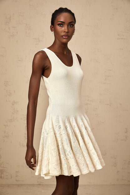 Woman wearing a short white textured knit dress with intricate jacquard pattern standing against plain background