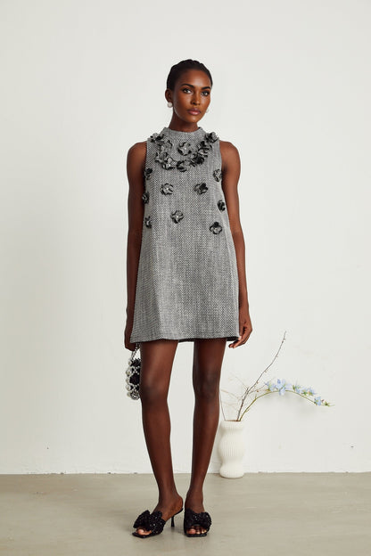 Woman wearing a sleeveless mini dress adorned with colorful faux flowers on a light background