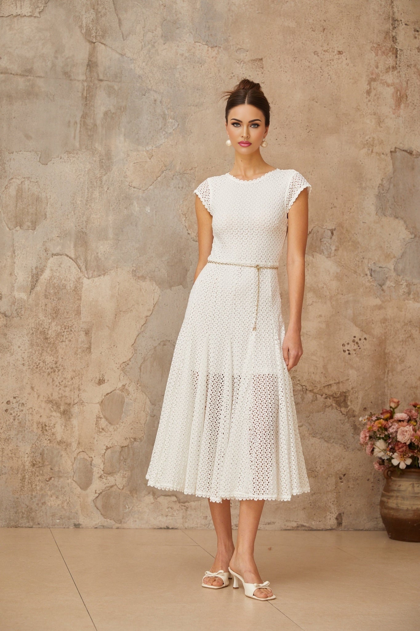 Woman wearing a white crochet knit midi dress with shirred detailing standing against a plain background