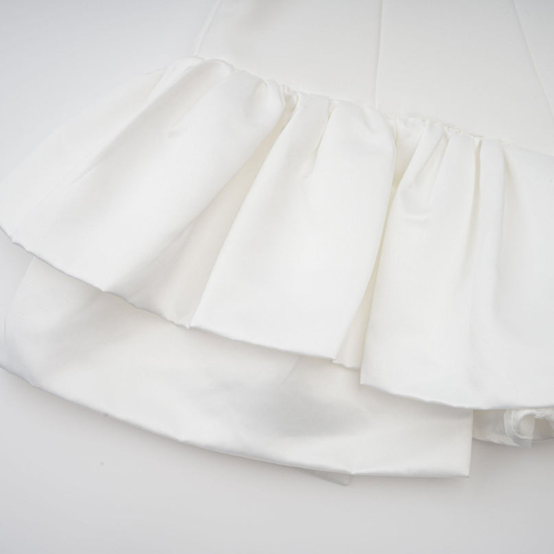 Woman wearing a white halterneck mini dress with ruffled details and a fitted silhouette