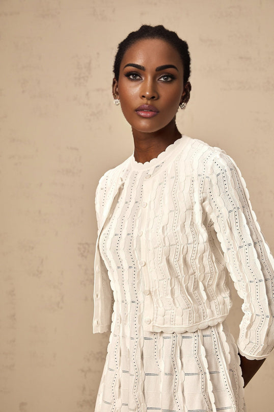 Woman wearing a white knitted cardigan with ruffled details and long sleeves