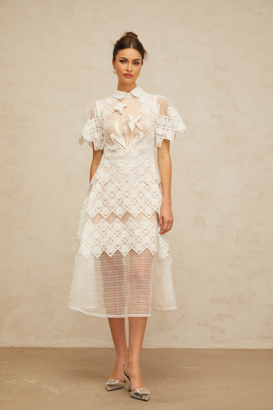 Woman wearing a white midi dress with floral embroidery details standing against a plain background