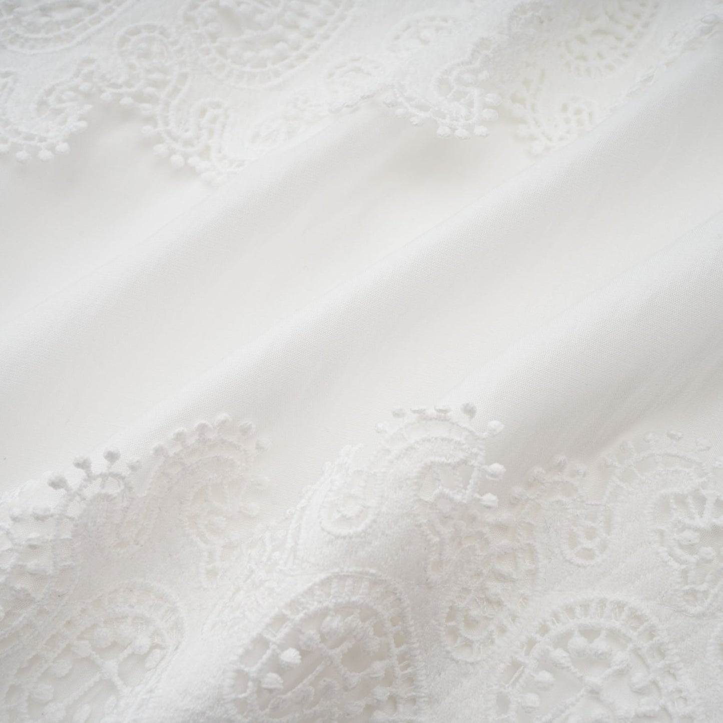 Woman wearing a white midi dress with lace trim panels and a belt at the waist