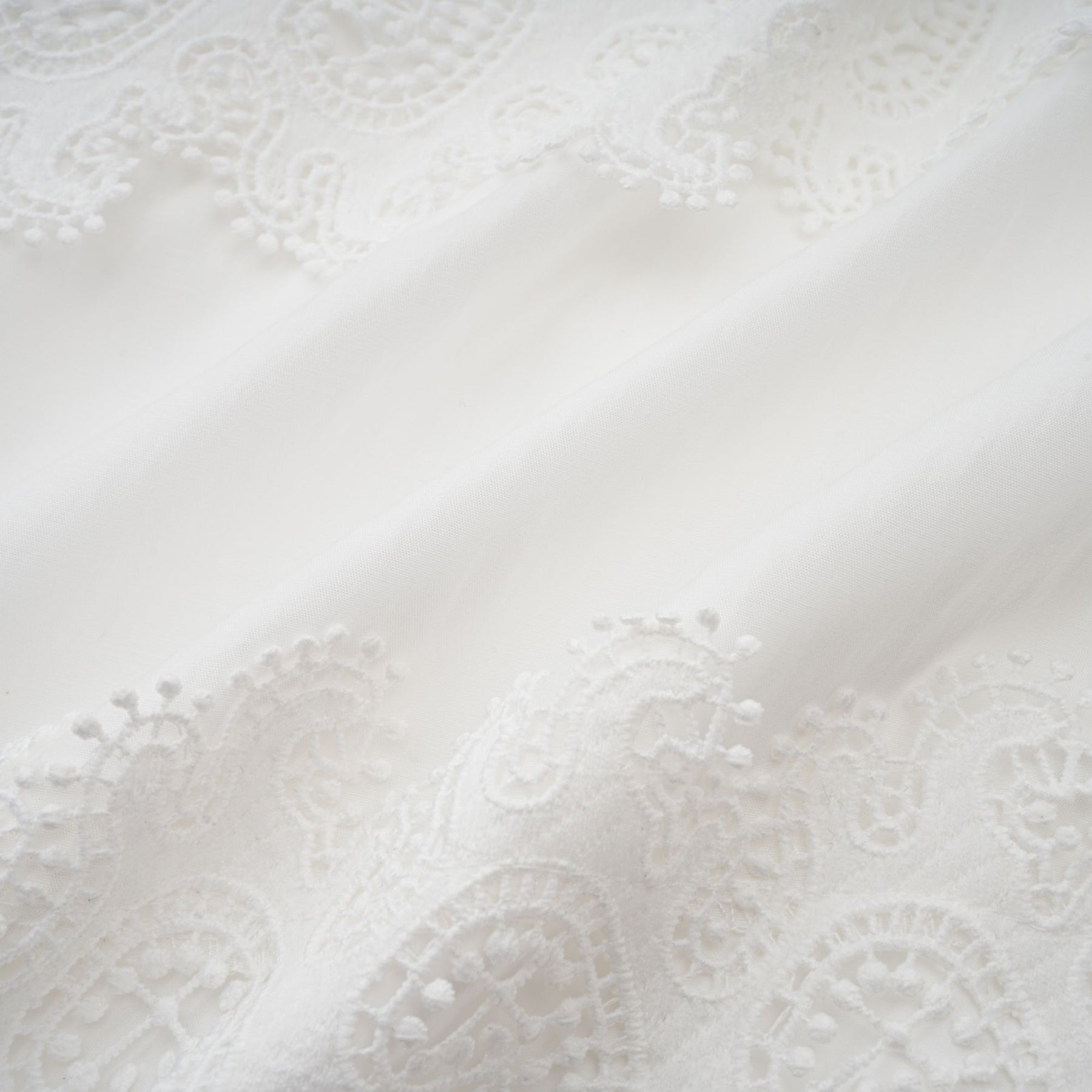 Woman wearing a white midi dress with lace trim panels and a belt at the waist