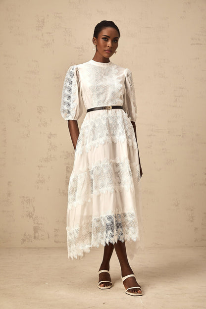Woman wearing a white midi dress with lace trim panels and a belt at the waist