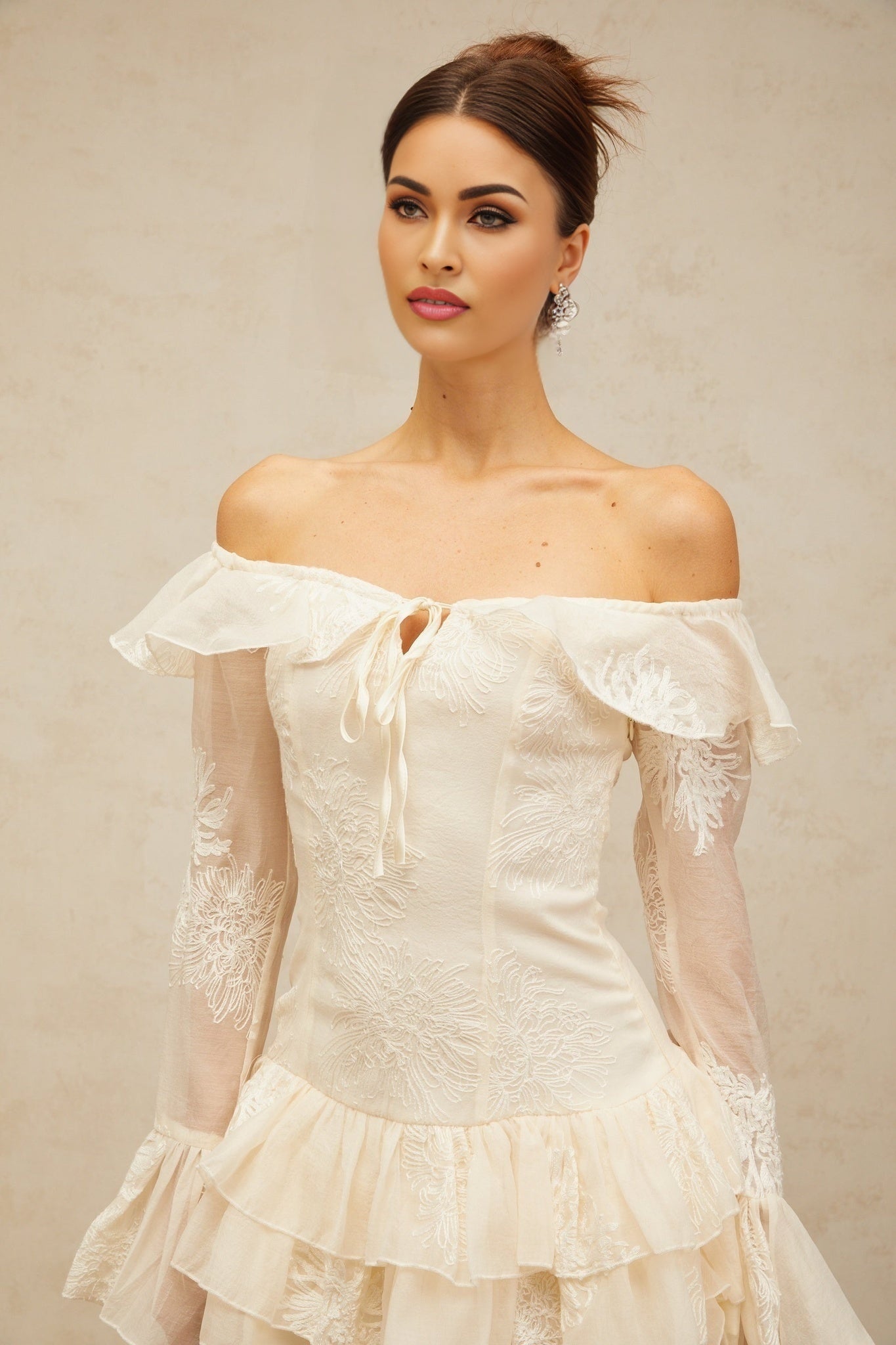 Woman wearing a white offshoulder mini dress with embroidery details standing against a plain background