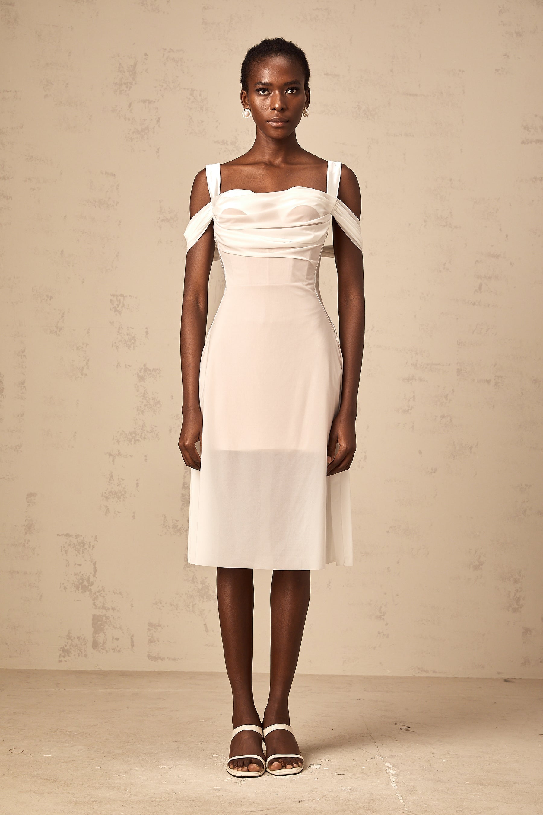 Woman wearing a white semi sheer ruched midi dress with gathered fabric details standing in a relaxed pose