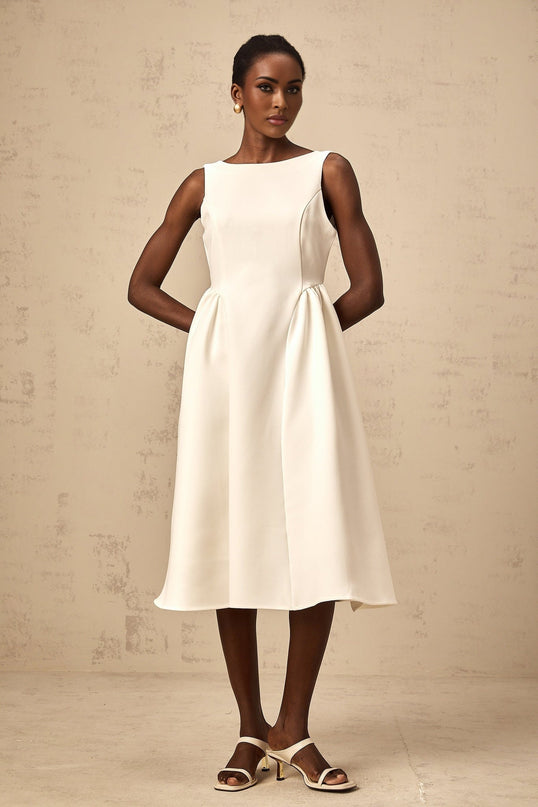 Woman wearing a white sleeveless midi dress with a full skirt standing against a plain background