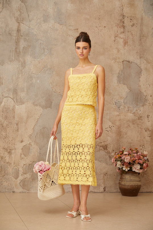 Woman wearing a yellow crochet knit matching set with sleeveless top and midi skirt standing against plain background