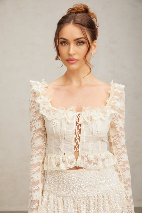 Woman wearing an off white blouse with floral lace pattern and ruffled details