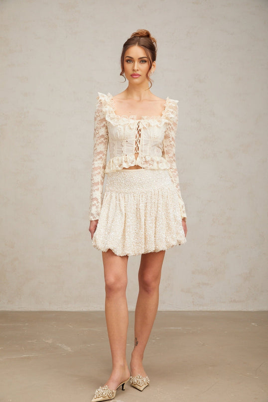 Woman wearing an off white blouse with floral lace pattern and ruffled details