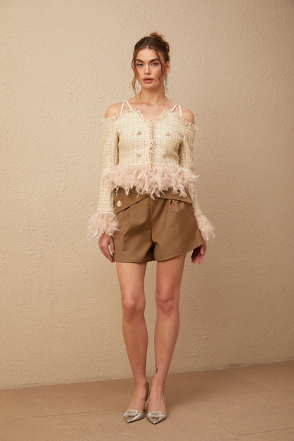 Woman wearing an offshoulder tweed top with feather trim along the neckline and sleeves in a light color