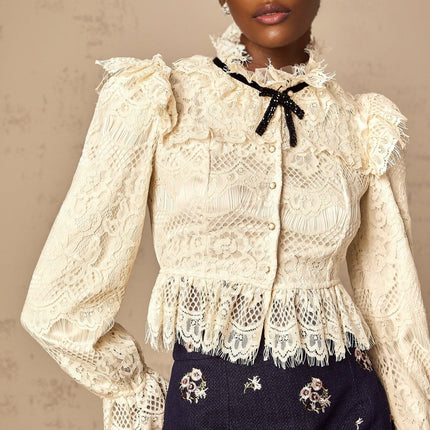 Woman wearing an offwhite blouse with floral lace pattern and bow detail at neckline
