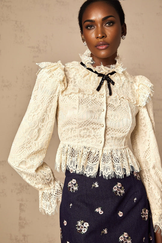Woman wearing an offwhite blouse with floral lace pattern and bow detail at neckline