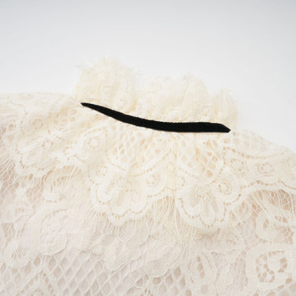 Woman wearing an offwhite blouse with floral lace pattern and decorative bowknot detail