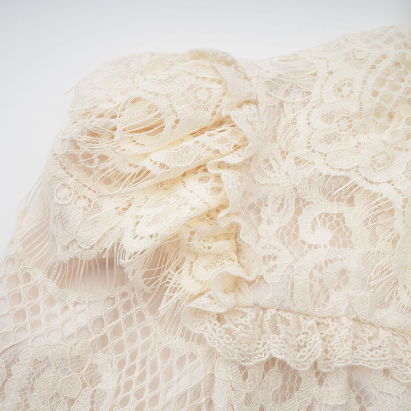 Woman wearing an offwhite blouse with floral lace pattern and large bow detail at neckline