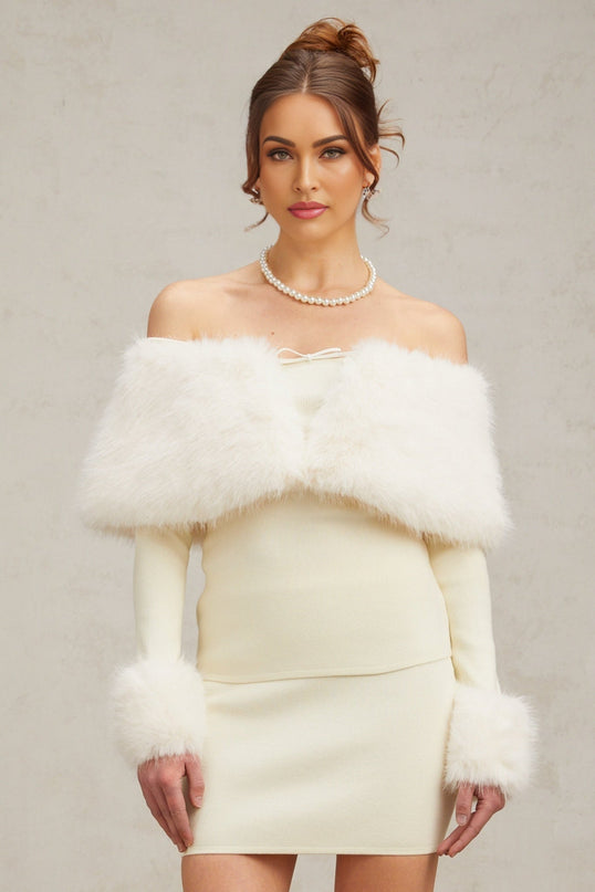Woman wearing an offwhite faux fur fine knit top and matching skirt set standing against a plain background