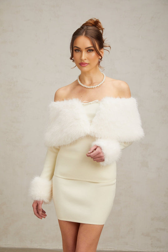 Woman wearing an offwhite faux fur fine knit top and matching skirt set standing against a plain background