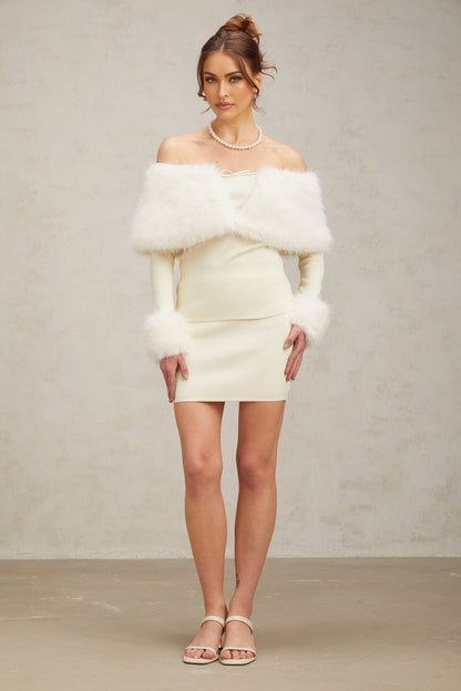 Woman wearing an offwhite faux fur fine knit top and matching skirt set standing against a plain background